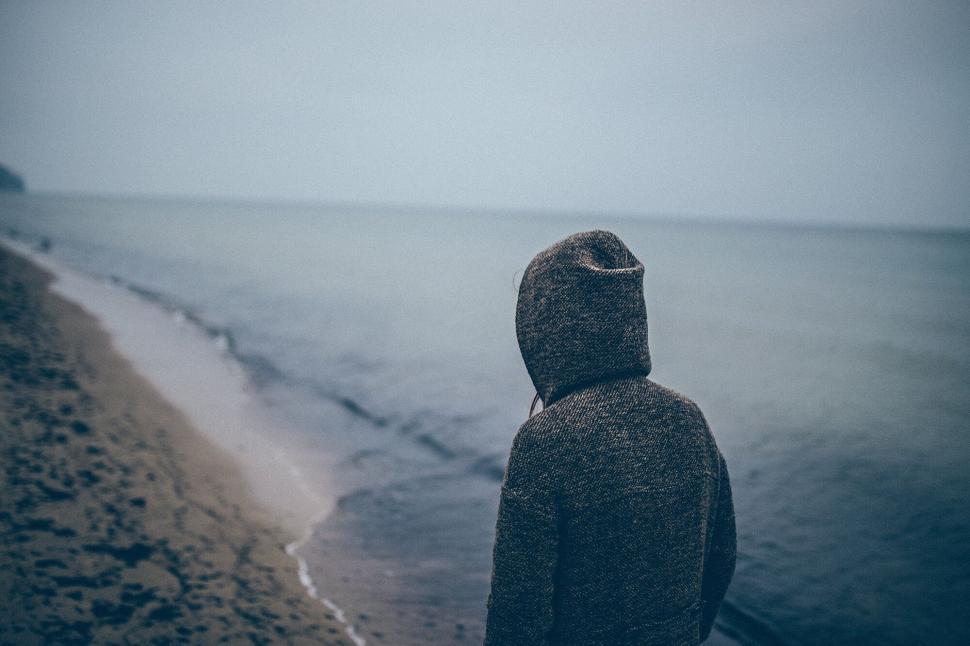 Free Image of Person in a hooded coat walks alone on a deserted beach 