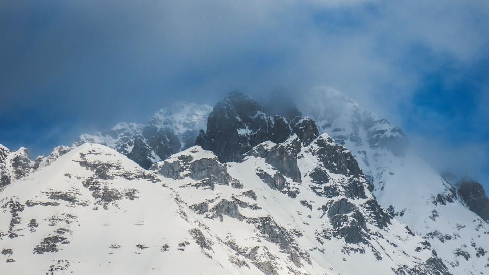 Free Image of Snow-covered mountain peaks under a cloudy blue sky 