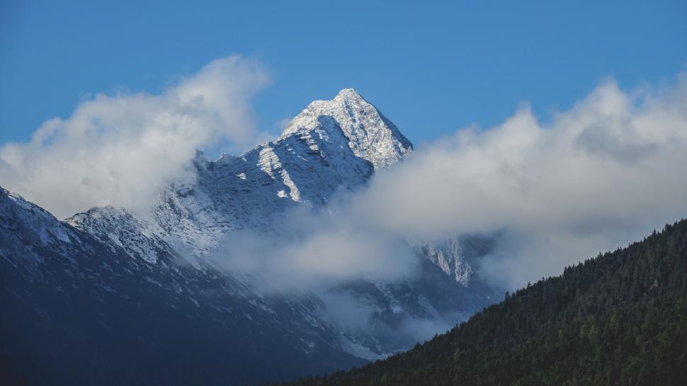 Free Image of Snow-covered mountain peak surrounded by cloudy sky. 