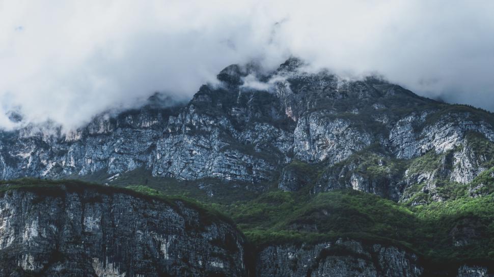 Free Image of Rocky mountain range with green foliage under cloudy sky 