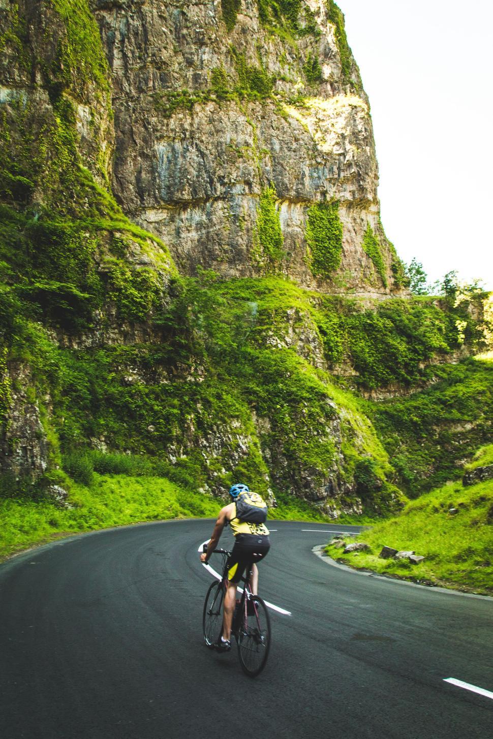 Free Image of Cyclist riding along a winding road through cliffs 