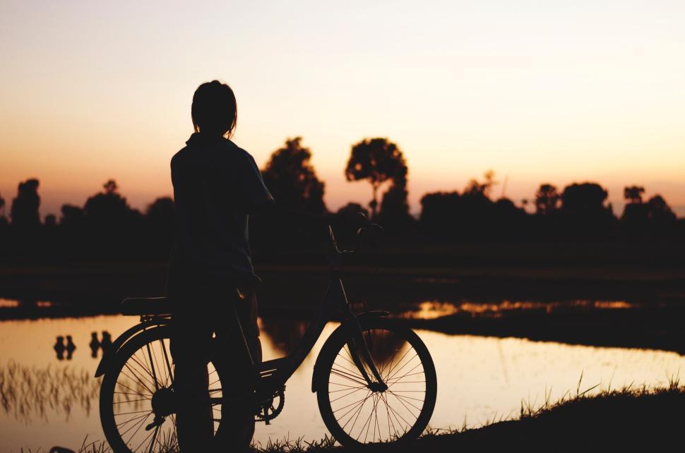 Free Image of Person with bicycle watching sunset near a calm lake 