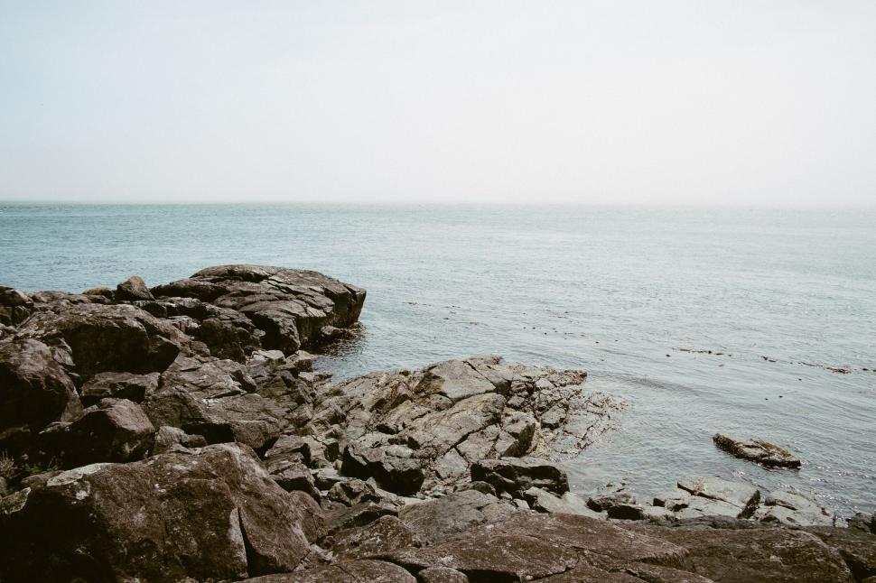 Free Image of Rocky seashore extends towards the calm, endless horizon 