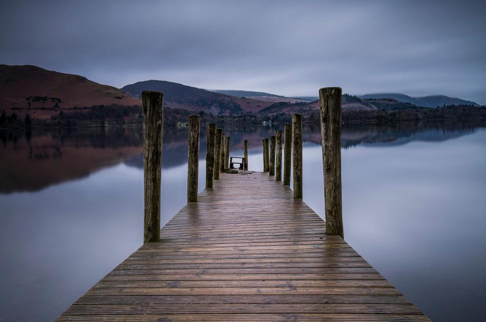 Free Image of Wooden pier extending into still lake under cloudy skies 