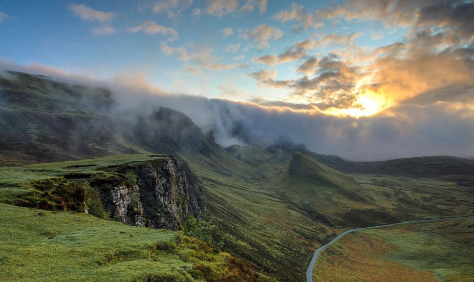 Free Image of Sunrise over green hills with mist and dramatic skies 