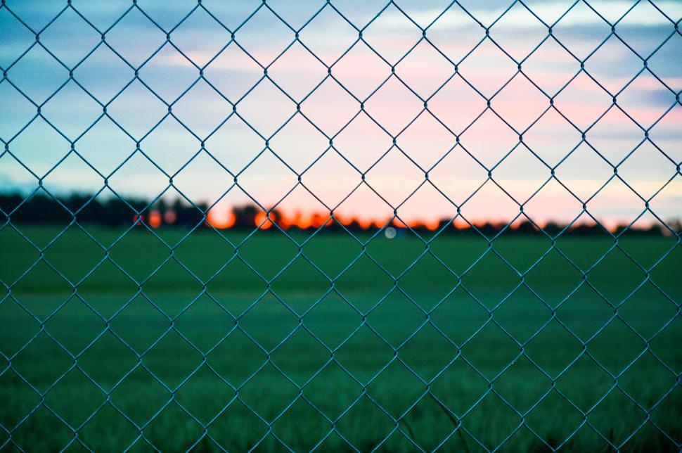 Free Image of Chain link fence with sunset in background over field 