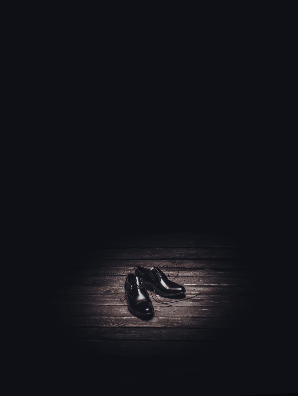 Free Image of Pair of black shoes on a dark wooden floor, spotlighted. 