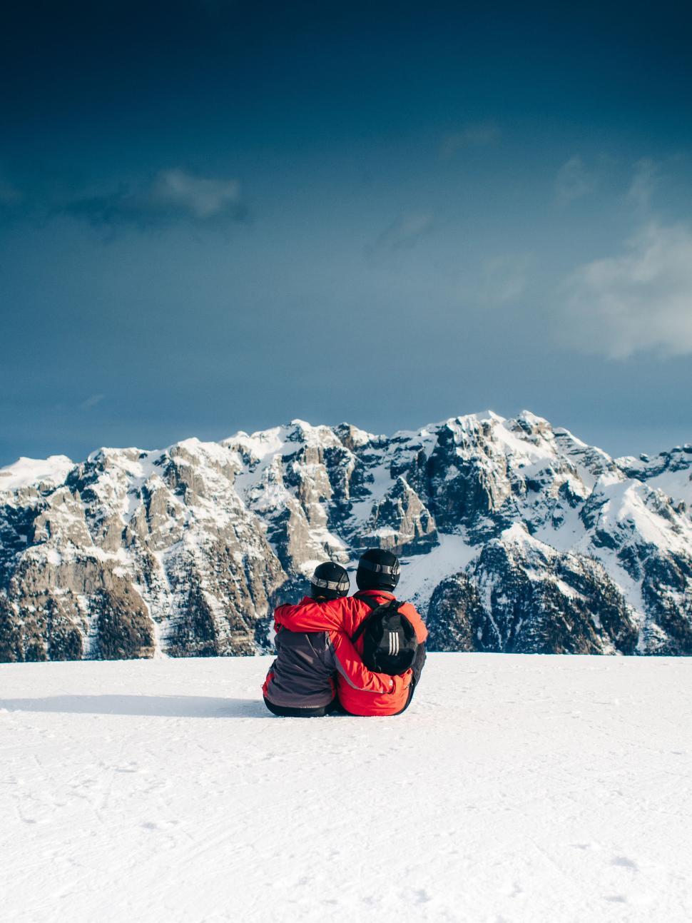 Free Image of Couple sitting on snowy mountain, embracing and gazing. 