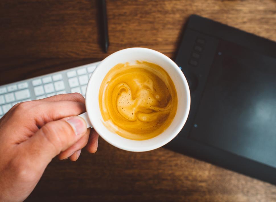 Free Image of Hand holding a cup of coffee above a wooden table. 