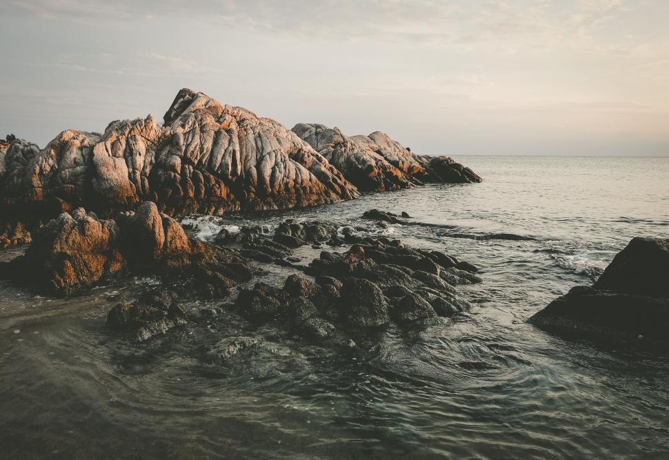 Free Image of Rocky beach shoreline with waves during sunset or sunrise. 