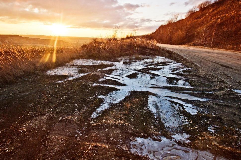 Free Image of Sunset over a rural road with icy puddles. 