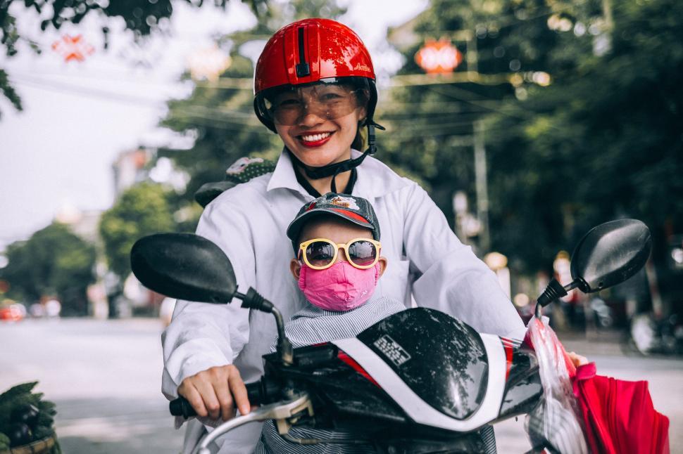 Free Image of Smiling woman and child on a scooter with safety gear 