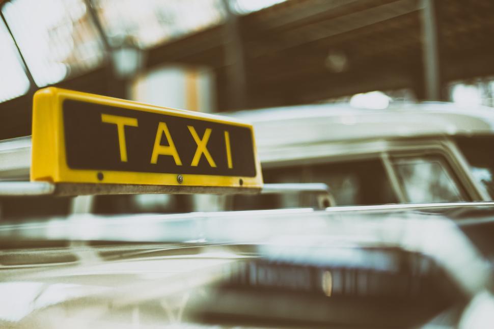 Free Image of Yellow taxi sign atop a car in an urban setting 