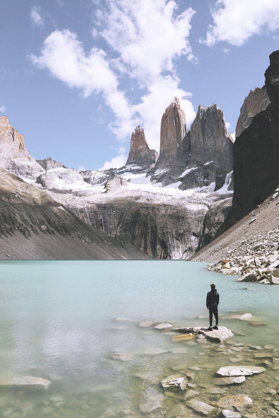 Free Image of Person standing by a lake with three towering peaks. 