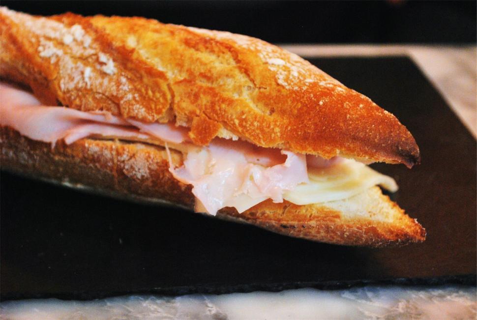 Free Image of Ham and cheese baguette sandwich on a dark surface. 