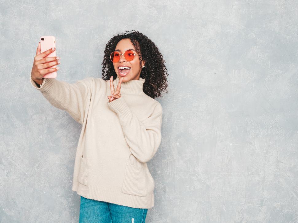 Free Image of Woman in beige sweater taking a selfie, peace sign 