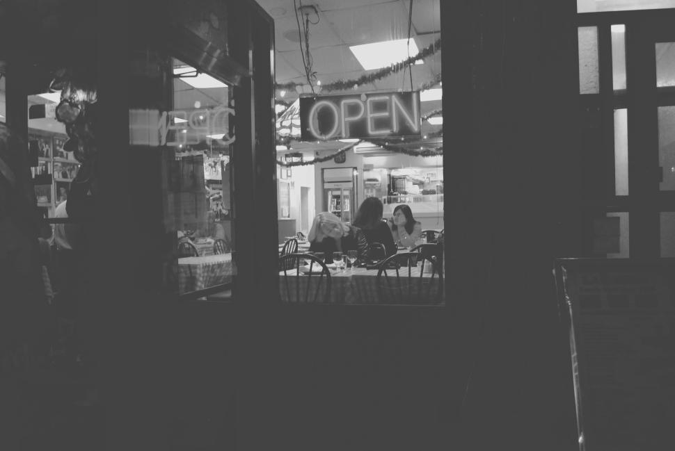Free Image of Cafe with an open sign and two patrons sitting inside 