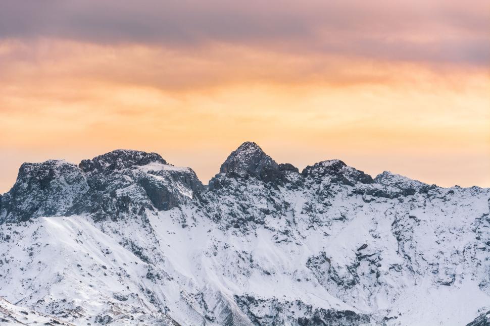 Free Image of Snowy mountain peaks under a dramatic sunset sky. 