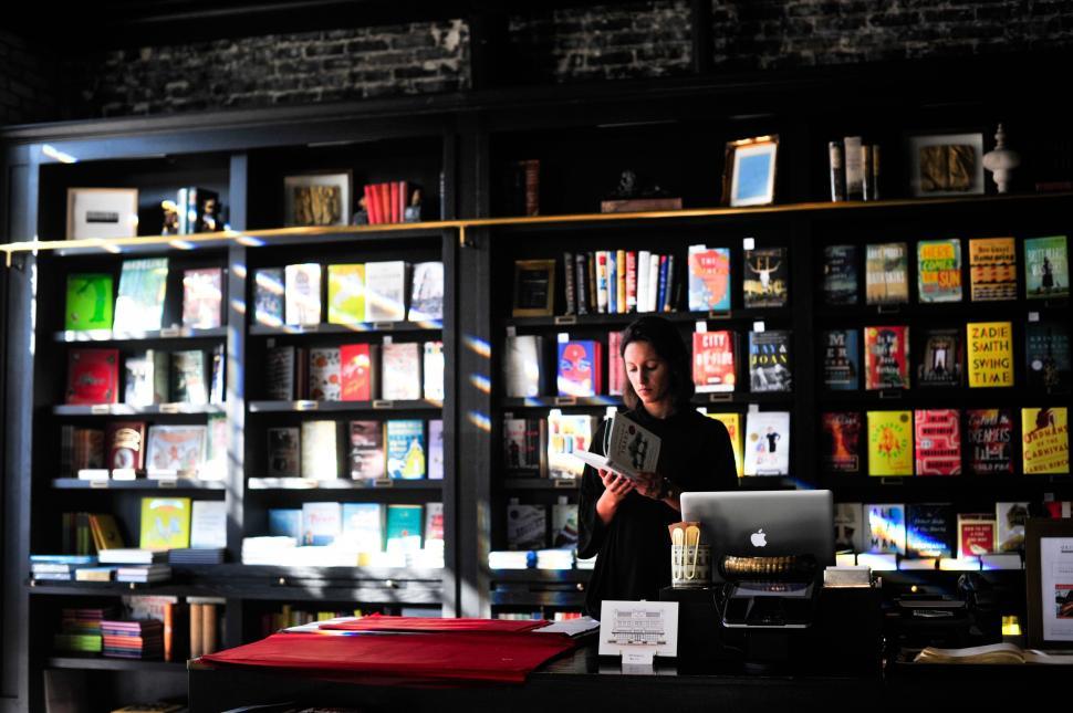 Free Image of Bookstore Clerk Reading a Book Behind the Countertop. 