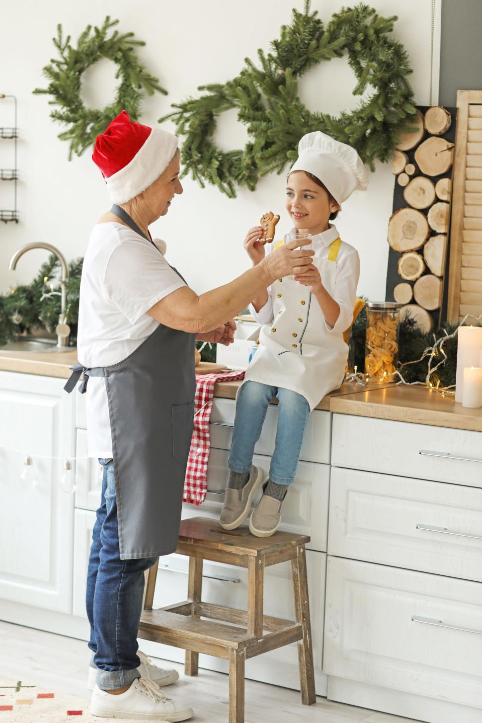 Free Image of Girl and grandmother toast cookies in holiday-themed kitchen 