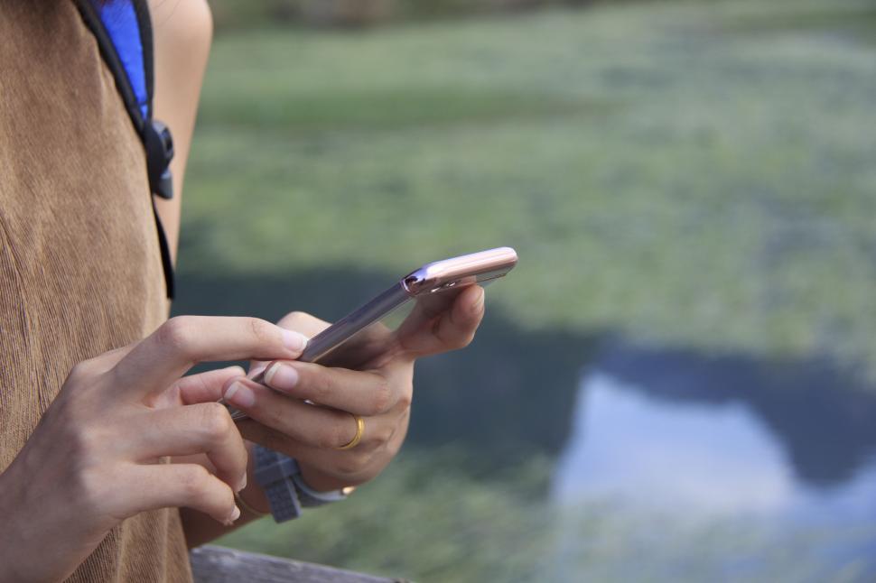 Free Image of Person using smartphone in the background of a lake. 