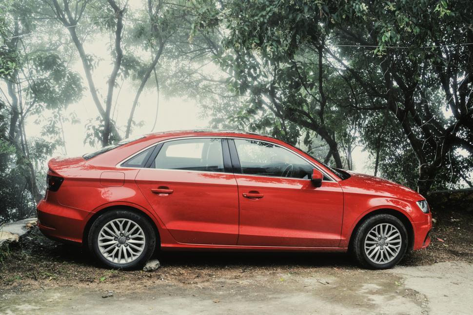 Free Image of A sleek red car parked in a lush green forest area 