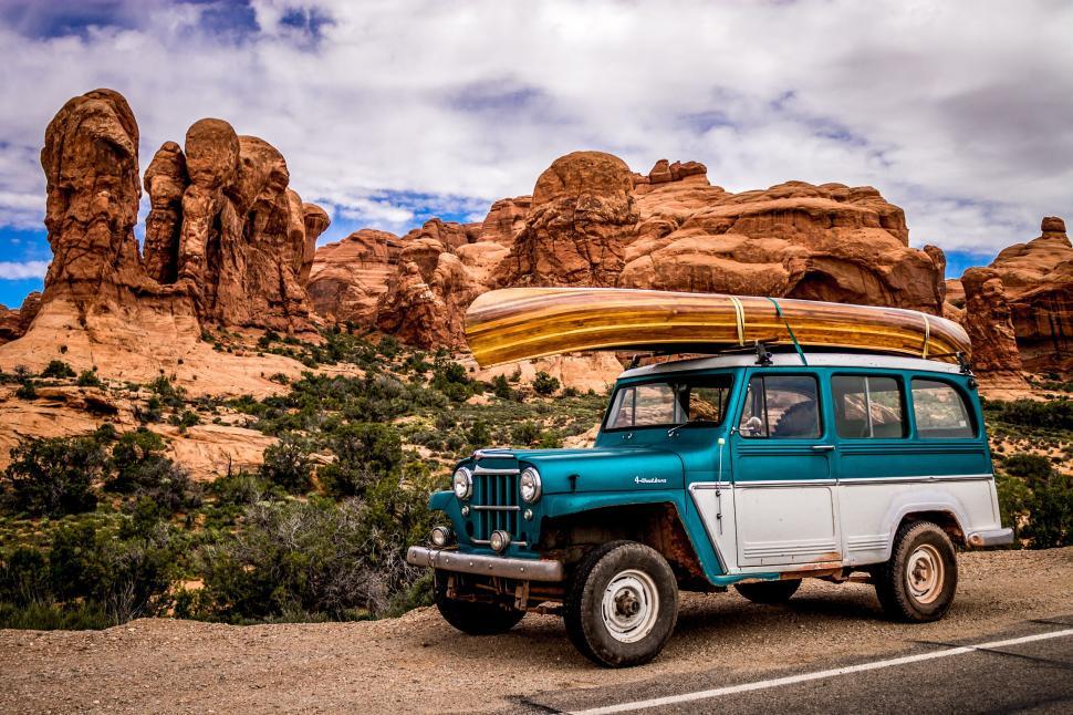 Free Image of Vintage blue vehicle with canoe near red rock formations. 