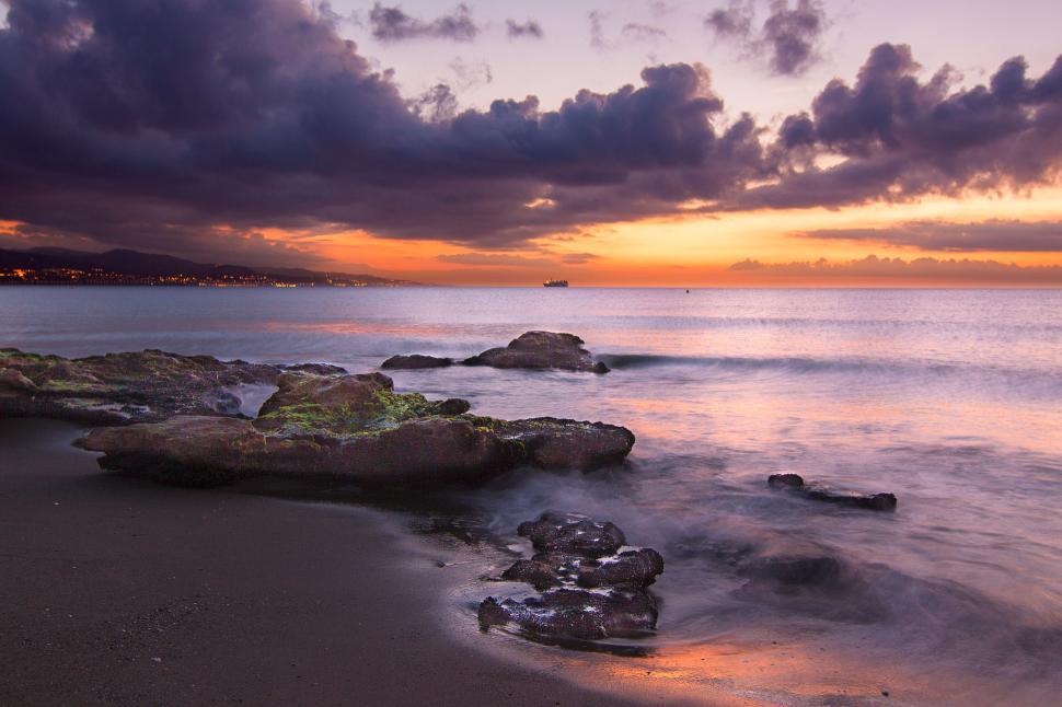 Free Image of Sunset over a rocky sea shore with a serene sky. 