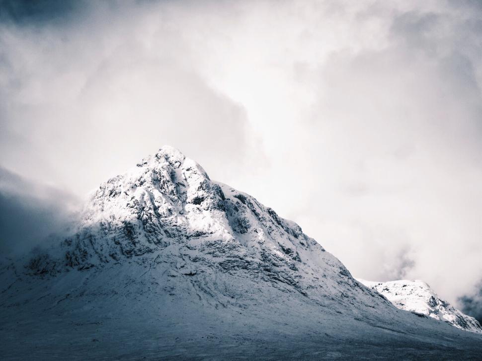 Free Image of Snow-covered mountain peak under a dramatic cloudy sky. 