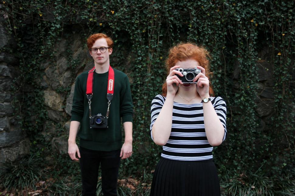 Free Image of Two individuals with vintage cameras in an outdoor setting 