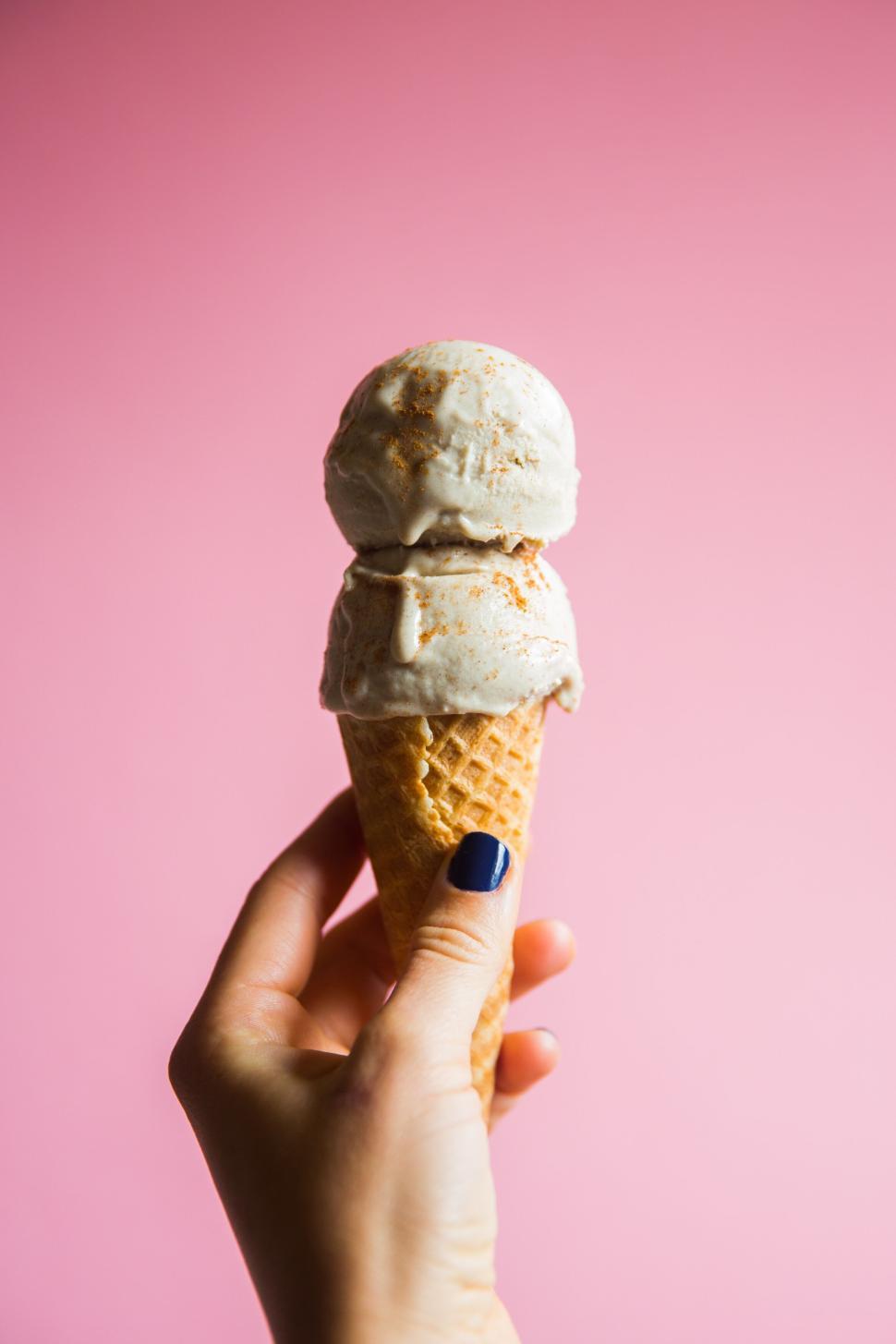 Free Image of Hand holding ice cream cone against a pink backdrop. 