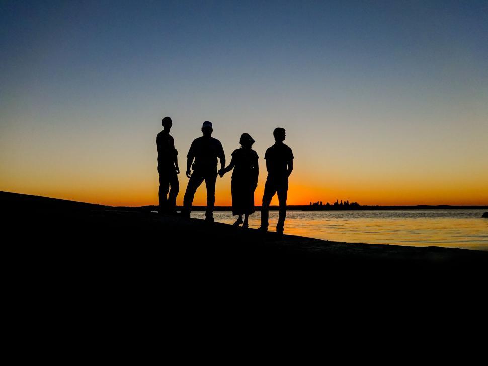 Free Image of Five people silhouetted against sunset along shoreline 