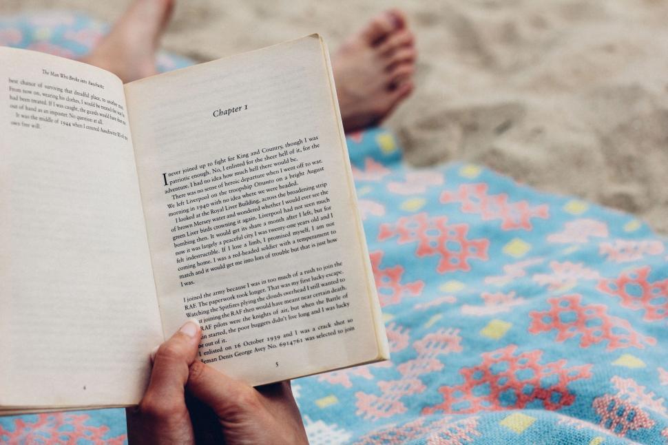 Free Image of Person reading book on a colorful blanket at beach 