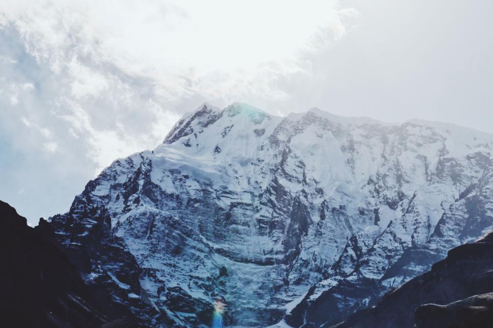 Free Image of Snow-covered mountain peak under bright sky, sun beams. 