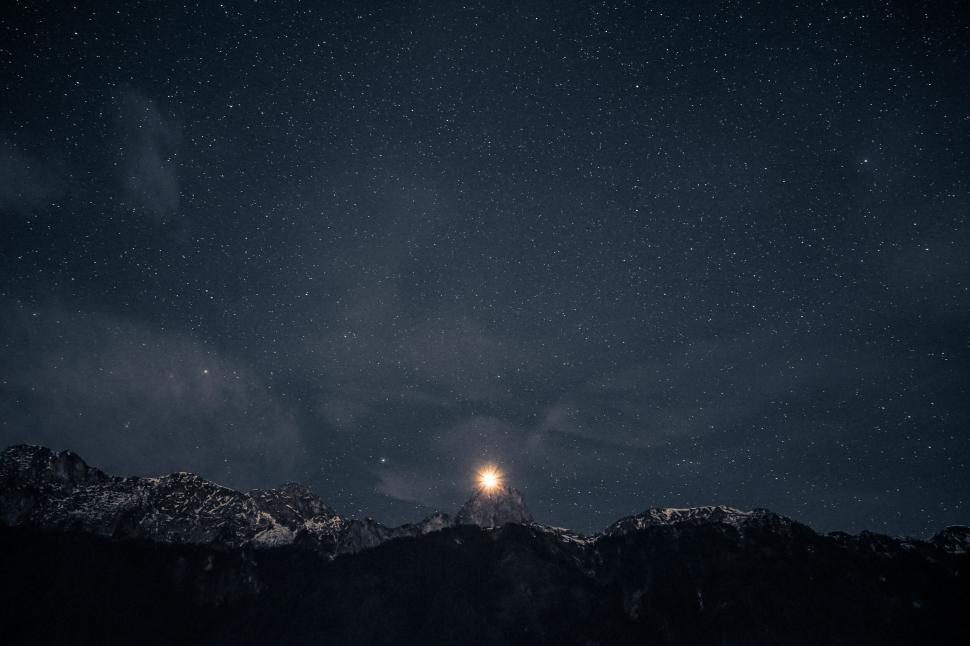 Free Image of Starry night sky over a mountain with a bright light. 