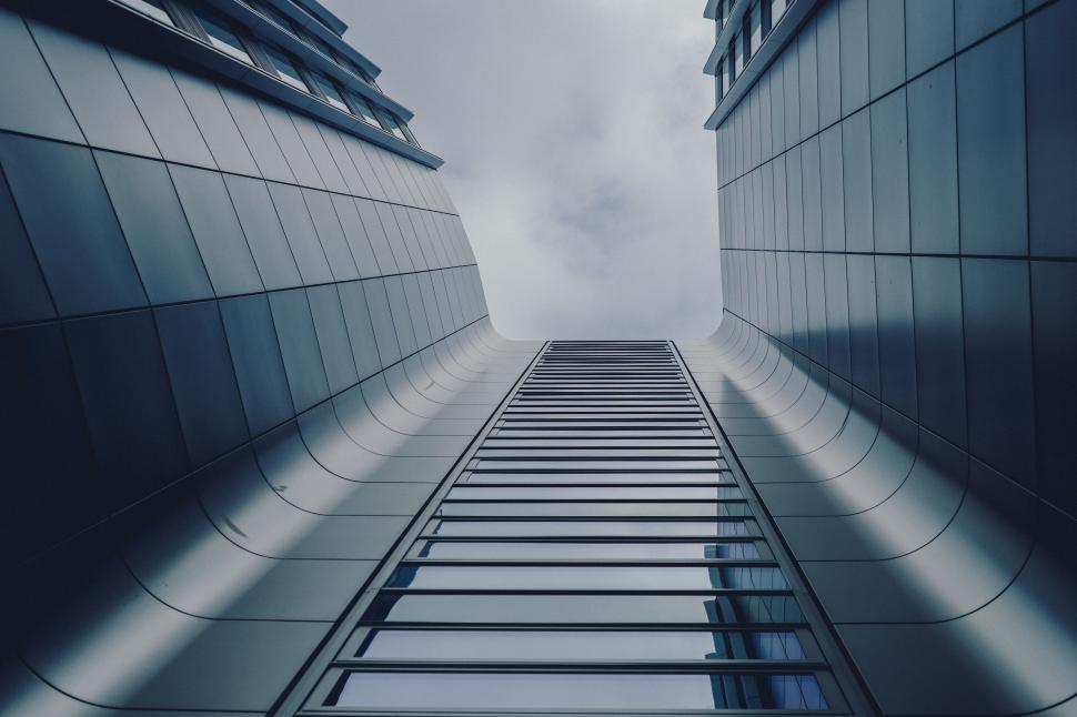 Free Image of Two tall buildings curving upwards under a cloudy sky 