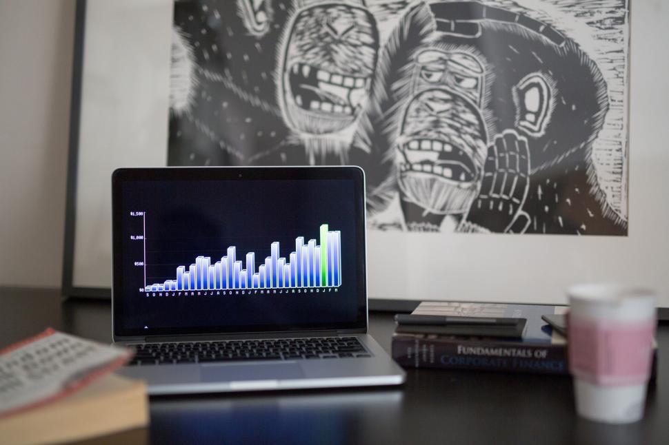 Free Image of Laptop showing graph with stacked books and coffee cups 