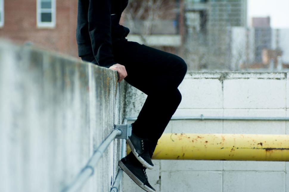 Free Image of Person seated on a concrete ledge, hands resting nearby rail 