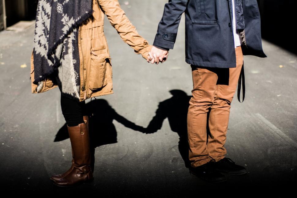 Free Image of Couple holding hands in coats standing on a city street 