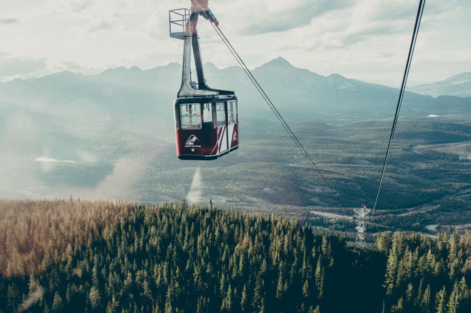 Free Image of Cable car high above a lush forest with mountains afar 
