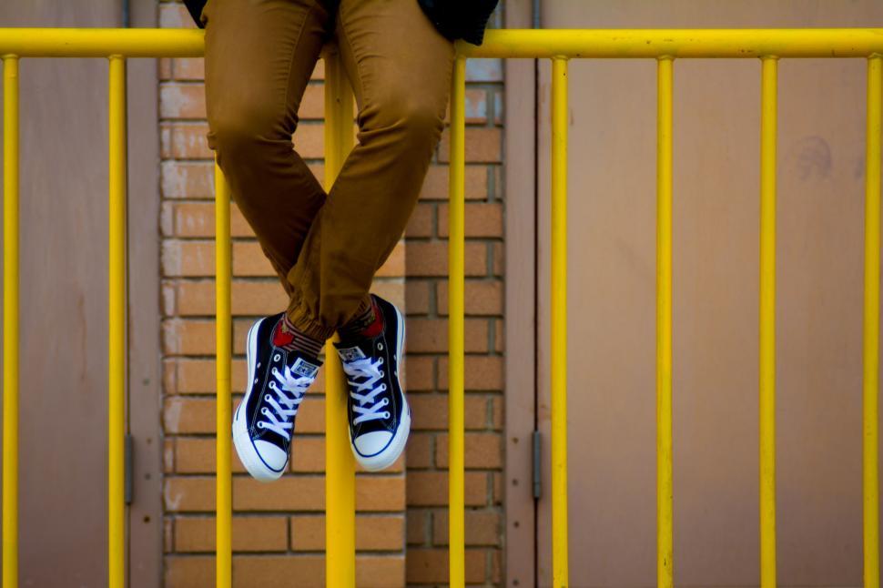 Free Image of Person sitting on yellow railing wearing black Converse shoes. 