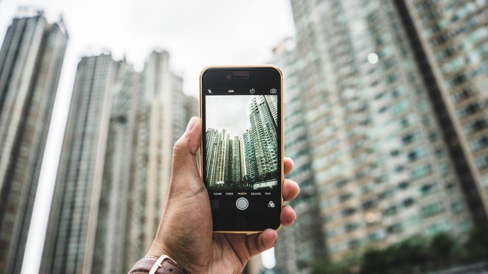 Free Image of Hand holding smartphone capturing tall urban buildings. 