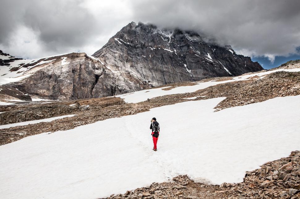 Free Image of A lone hiker walking on snowfield towards a tall mountain. 