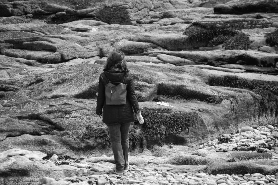 Free Image of Woman hiking amidst moss-covered rocks and pebbles. 