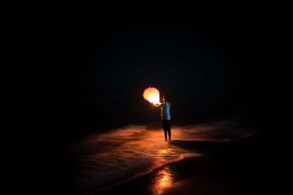 Free Image of Person releasing a lantern on a beach at nighttime 