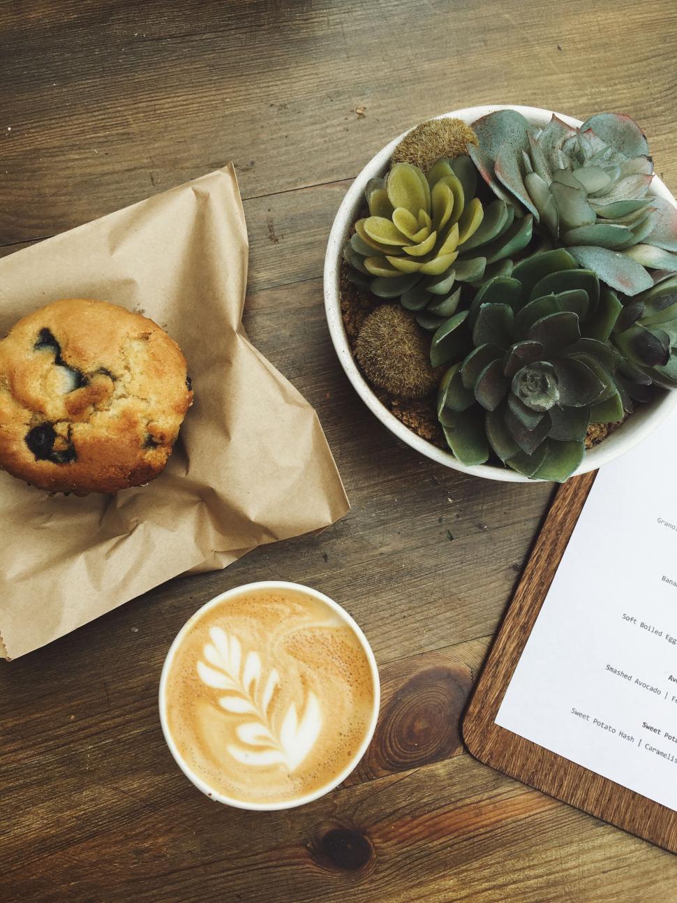 Free Image of Latte with foam art beside muffin and succulents. 