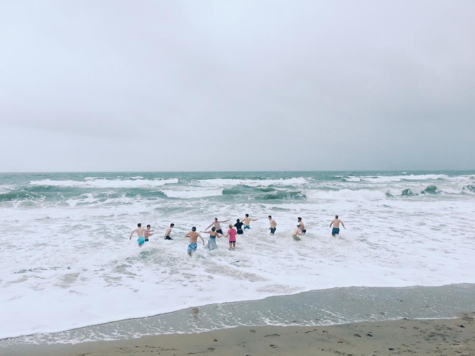 Free Image of Group of people splash in ocean waves on sandy beach. 