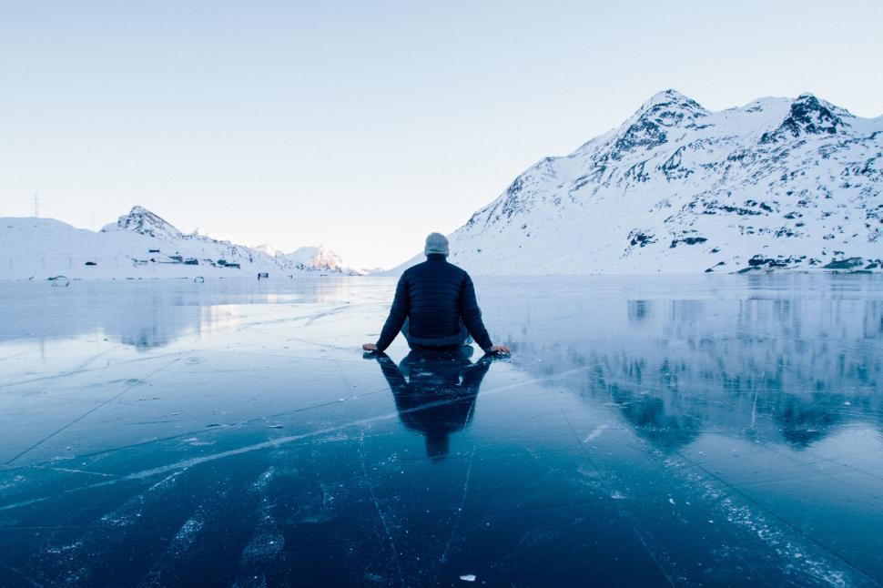 Free Image of Person sitting on frozen lake amidst snowy mountains. 