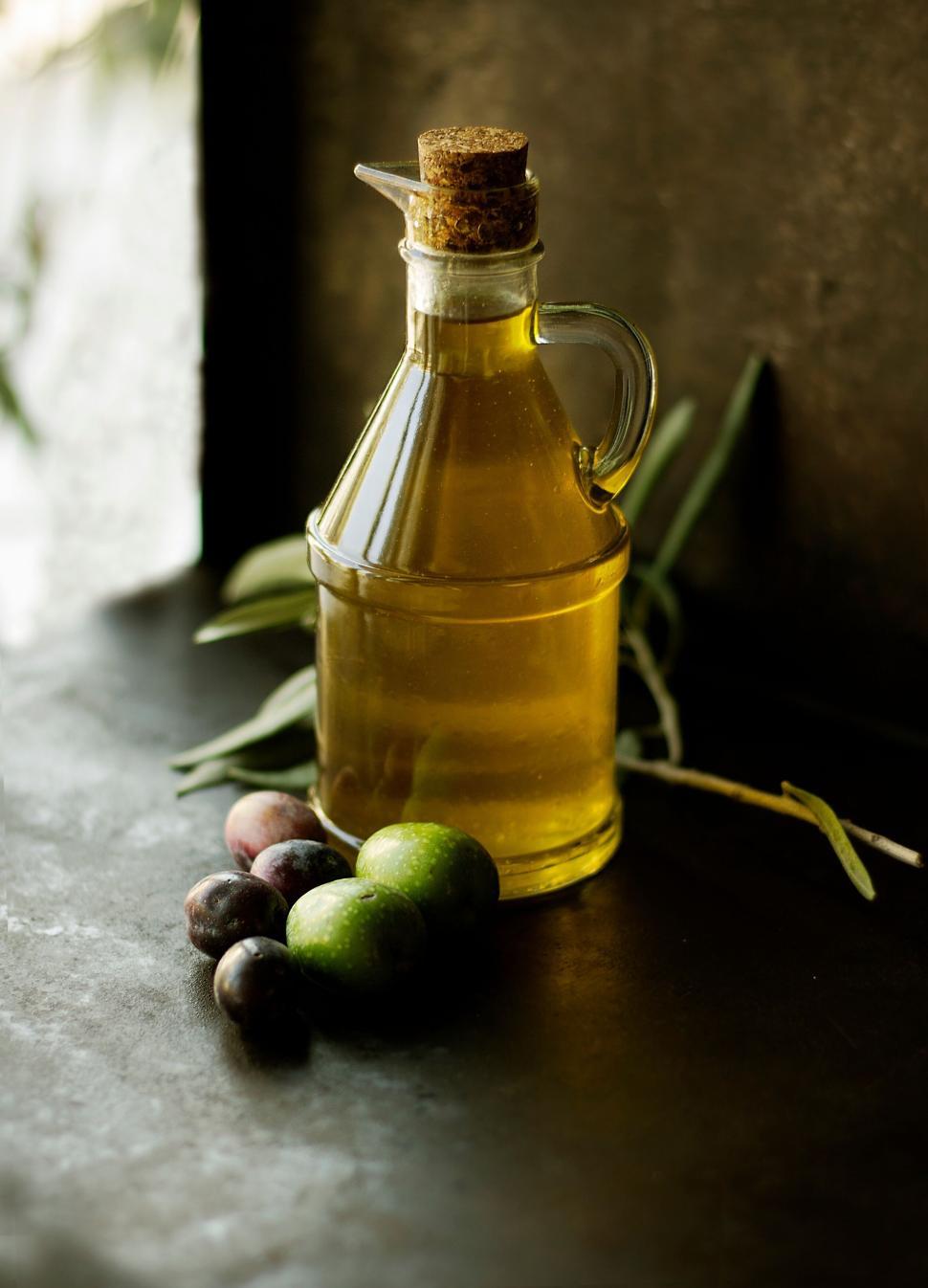 Free Image of Glass bottle of olive oil with olives on a dark surface 
