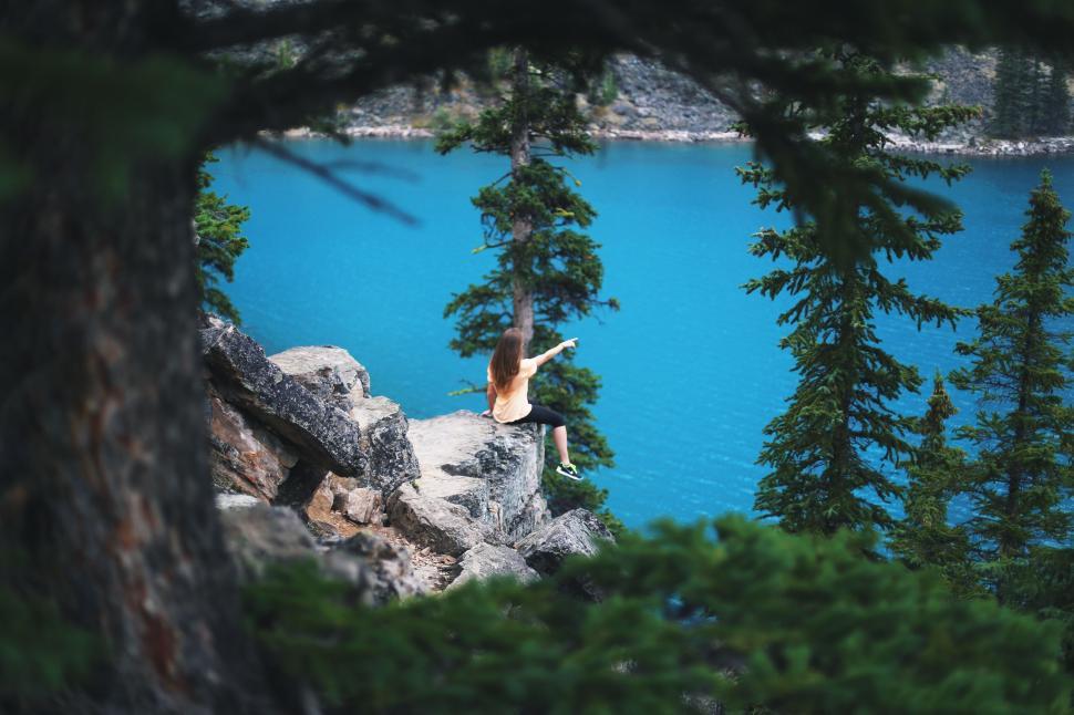 Free Image of Woman pointing from cliff overlooking crystal blue lake 